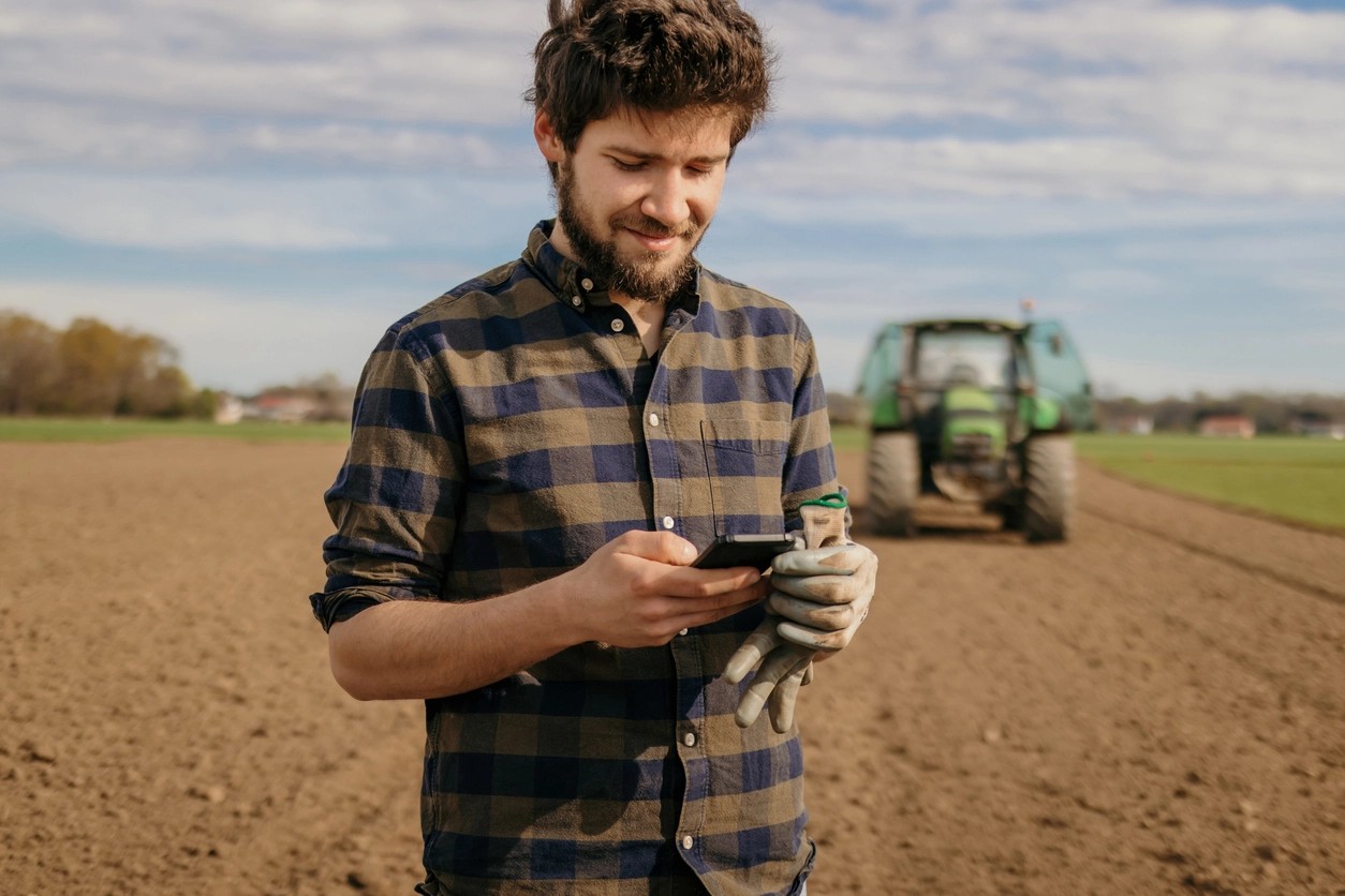 travailleur agricole consulte son téléphone devant son tracteur