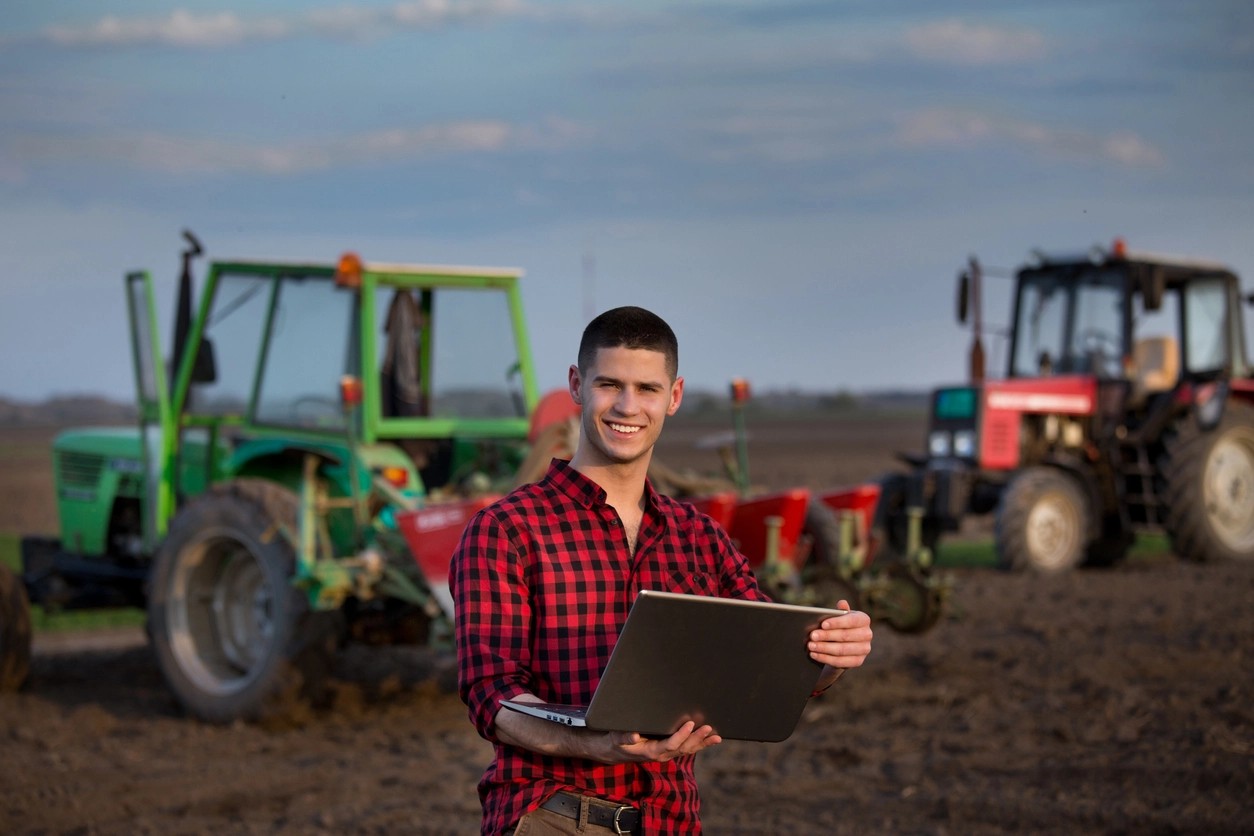 travailleur agricole sur son ordinateur devant les tracteurs