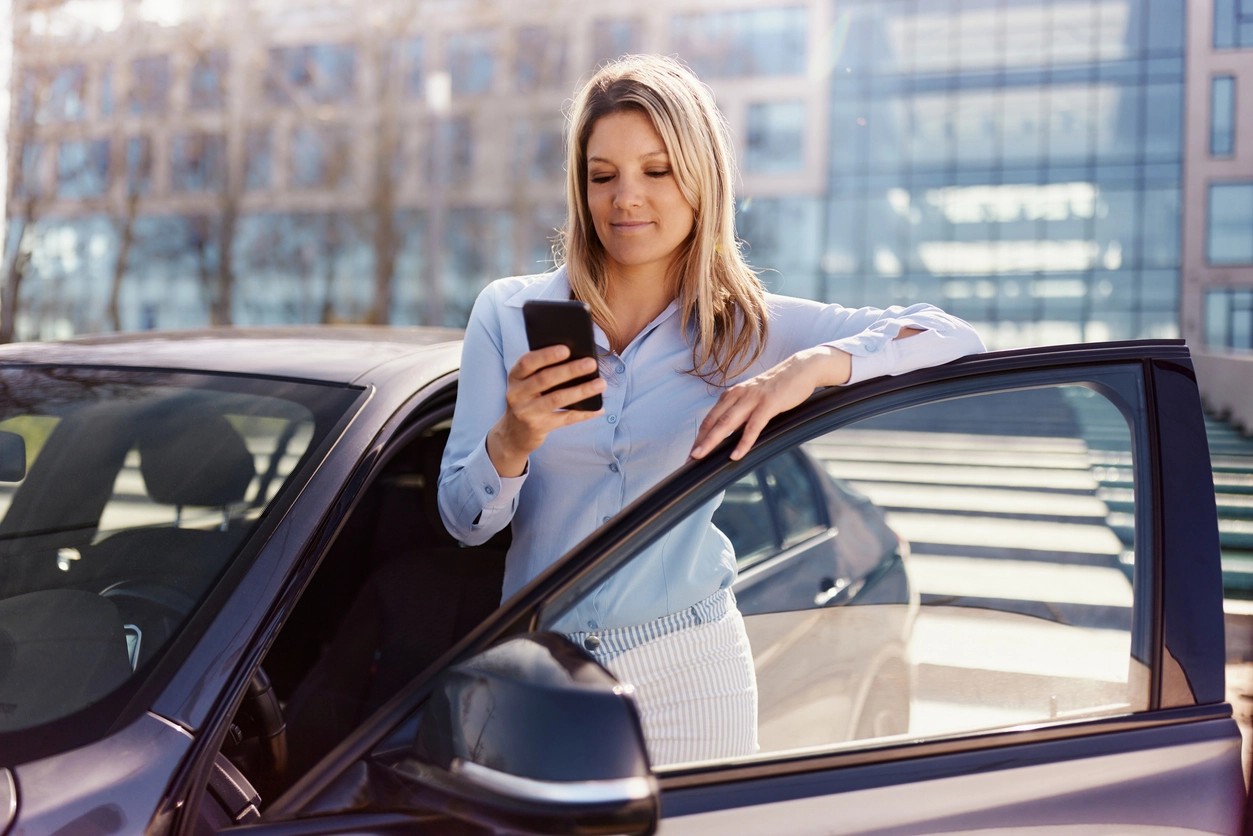 femme consultant son téléphone appuyée sur la portière de sa voiture